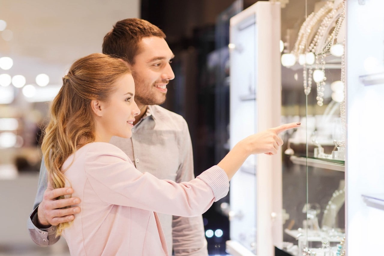 A smiling couple looking at a brightly lit jewellery display as the woman excitedly points at a piece.