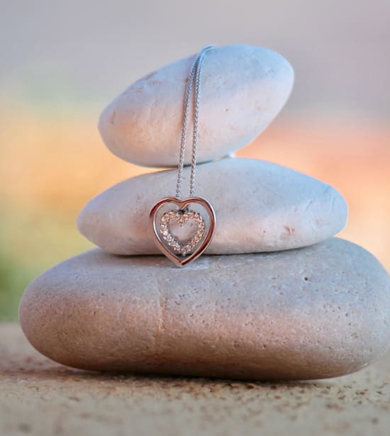 A beautiful heart necklace draped over a stack of three smooth stones