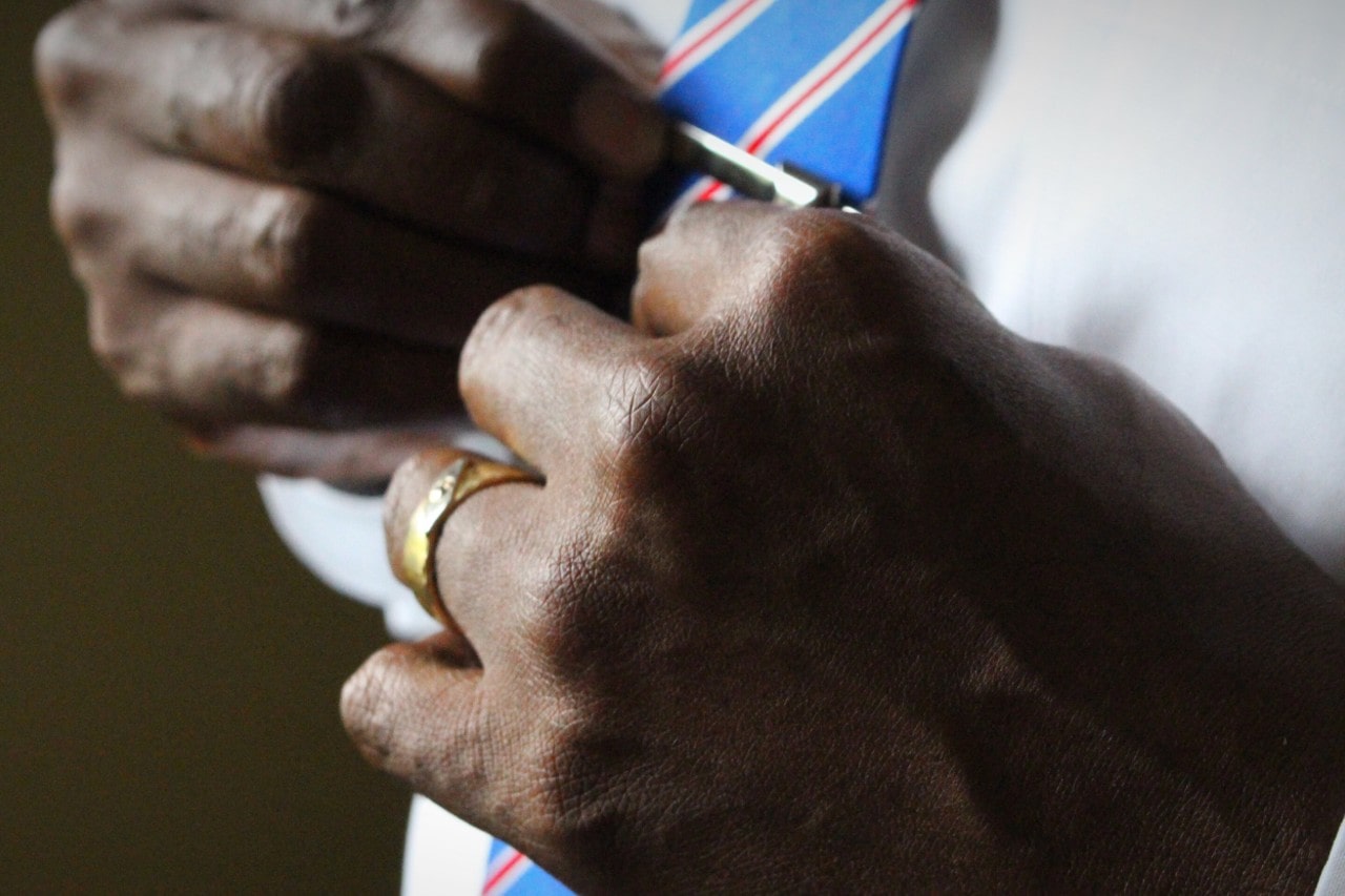 A close-up of a man’s hands as he adjusts his tie, with emphasis on his gold wedding band. A close-up of a man’s hands as he adjusts his tie, with emphasis on his gold wedding band.