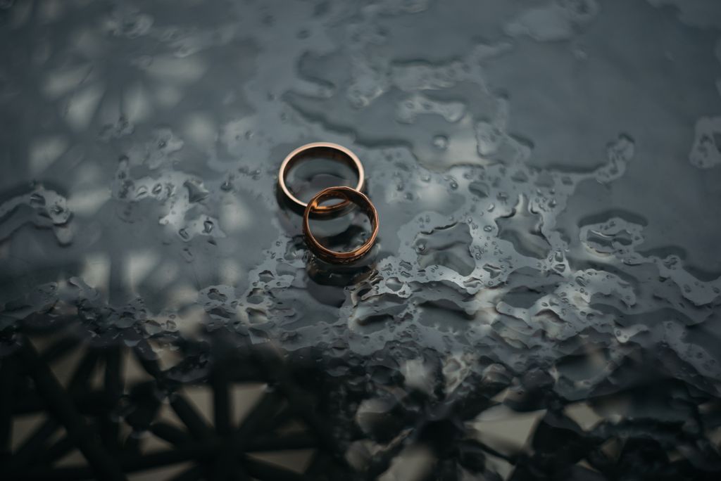 A top-down view of two bold wedding bands displayed one on top of the other on rain-covered glass. A top-down view of two bold wedding bands displayed one on top of the other on rain-covered glass.