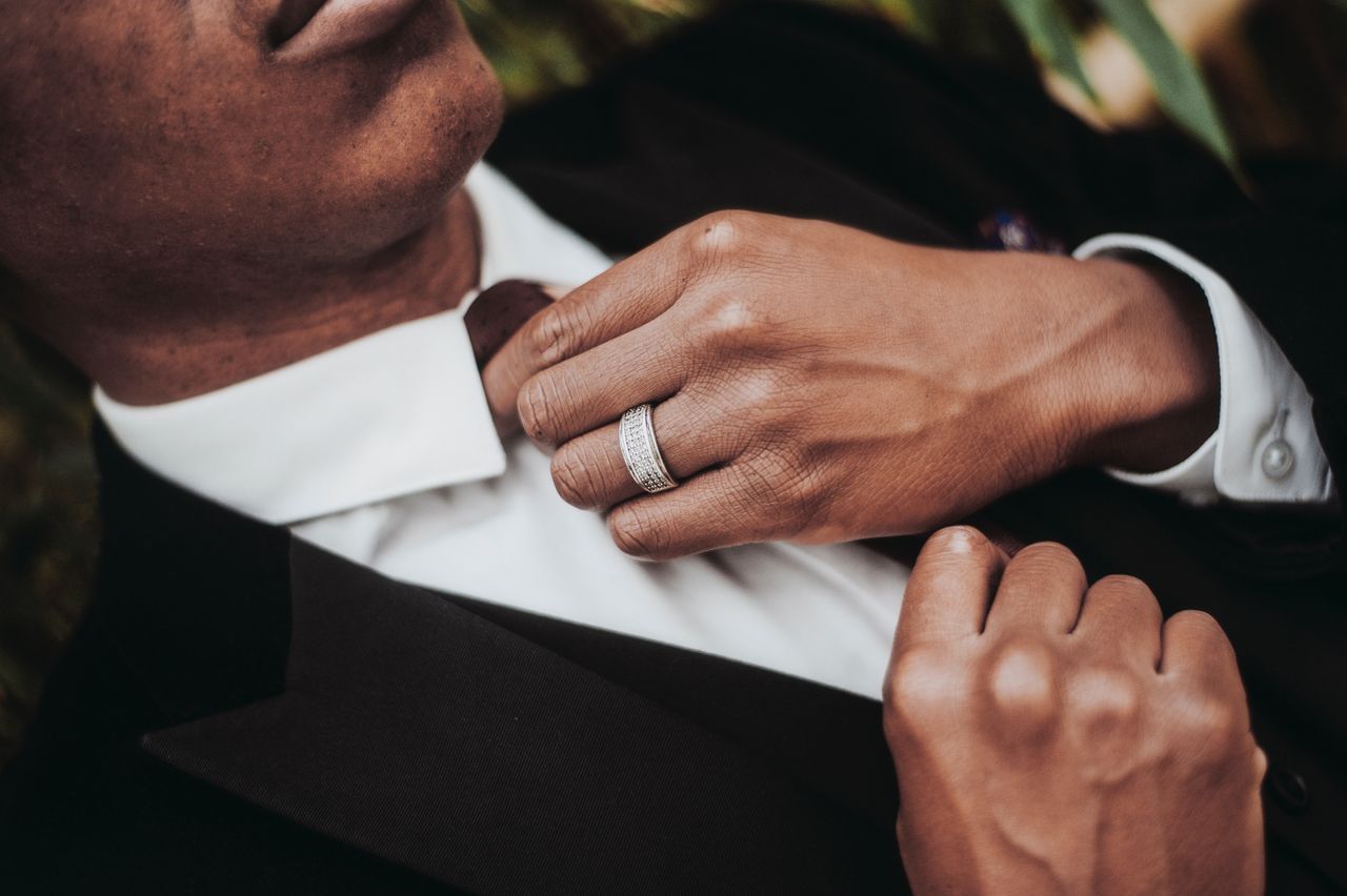 A close-up of a man in a suit straightening his tie, with emphasis on his elegant wedding band. A close-up of a man in a suit straightening his tie, with emphasis on his elegant wedding band.